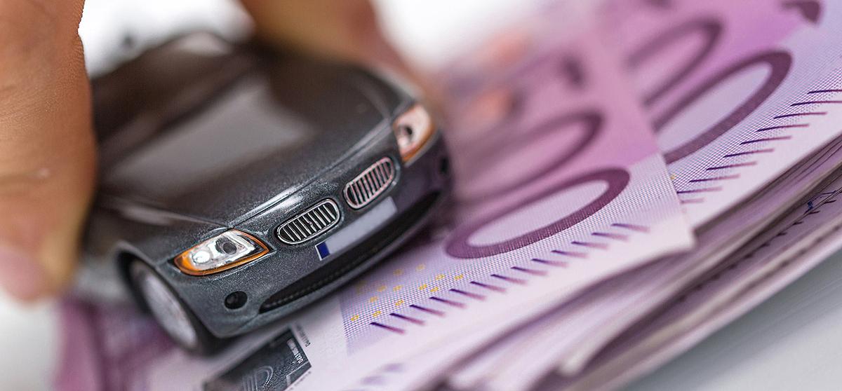 Spielzeugauto wird über einen Stapel Geldscheine geschoben