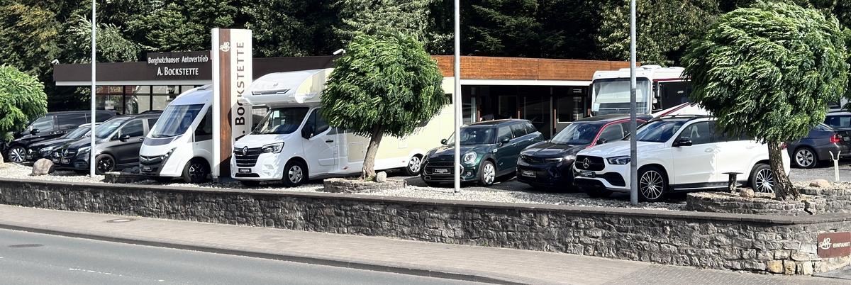 Teil der gepflegten, begünten und modernen Außenansicht von Autohaus Bockstette mit Autos und Reisemobilen auf dem Außenplatz