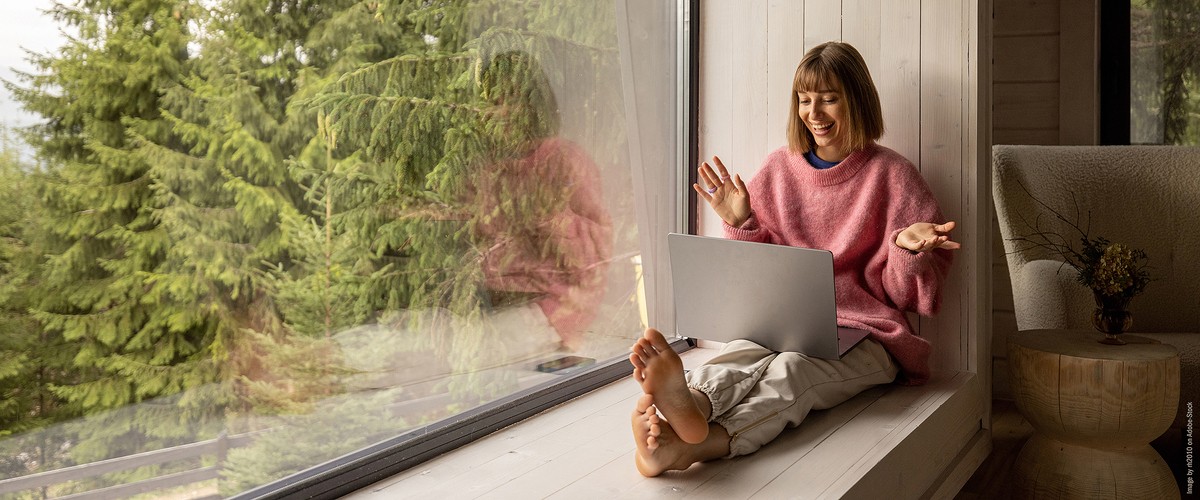 Frau sitzt am Fenster und freut sich über etwas in ihrem Laptop